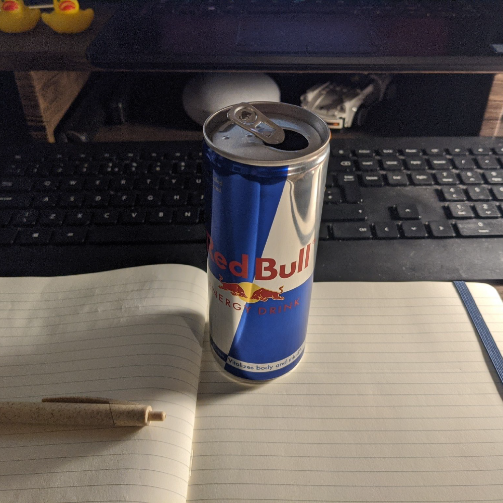 Red bull can on a desk near a keyboard and monitor.